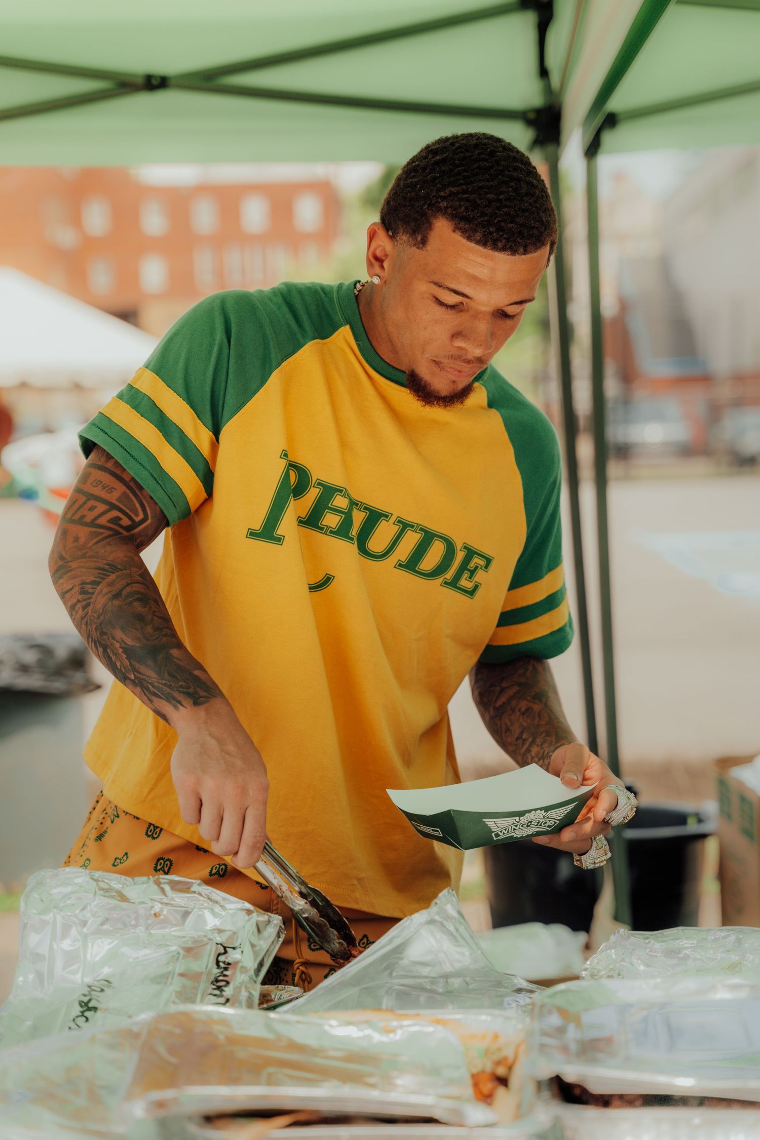 Chef in yellow and green uniform prepares food at outdoor kitchen table.