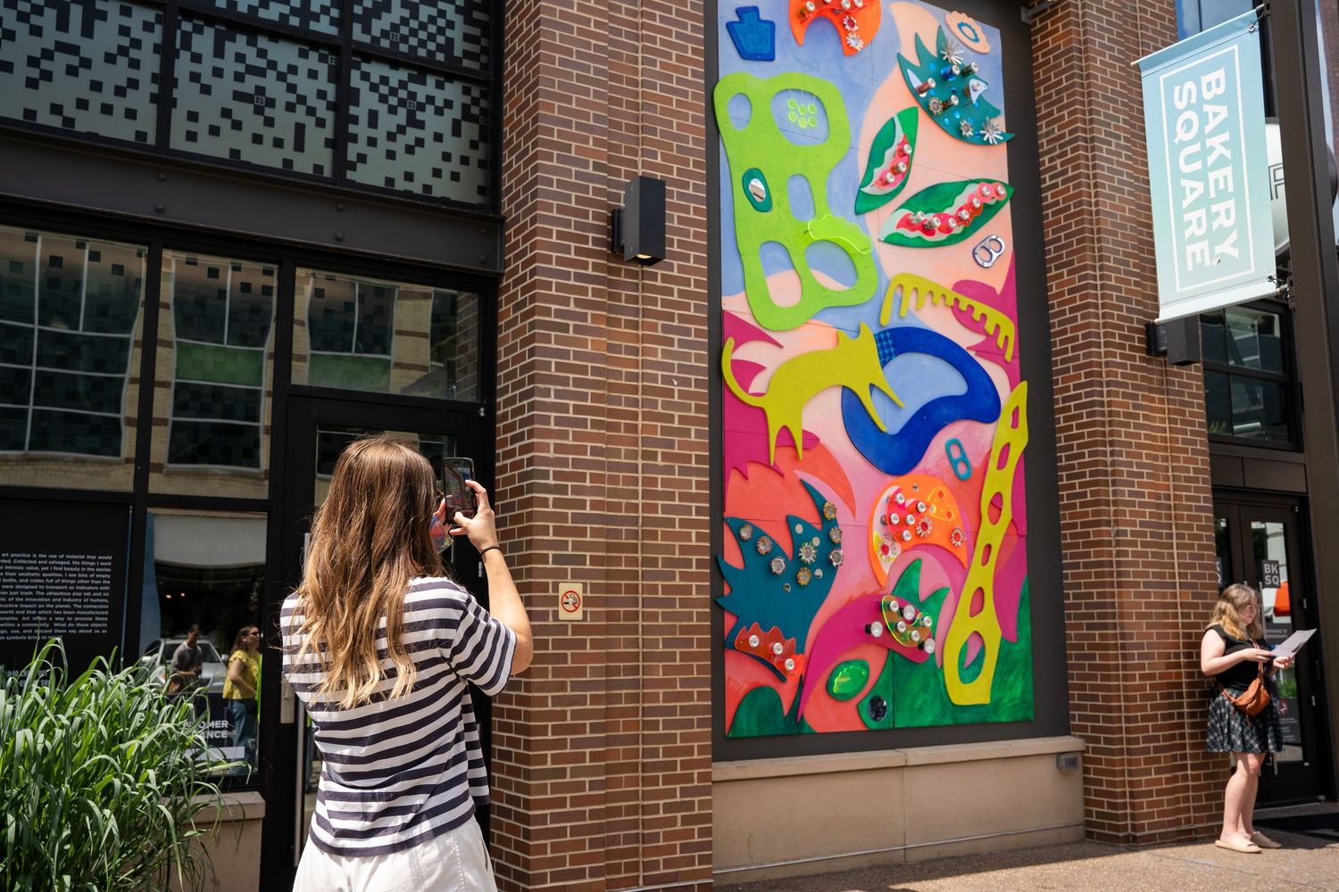 A person takes a photo of colorful abstract murals painted on brick walls outside a building.