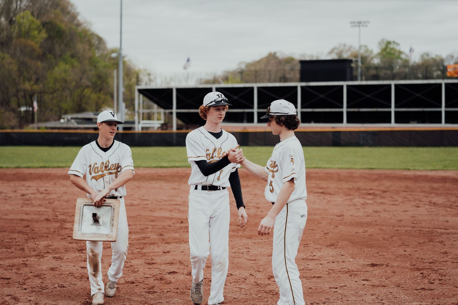 Baseball players in white uniforms celebrating on a dirt field after a successful play.