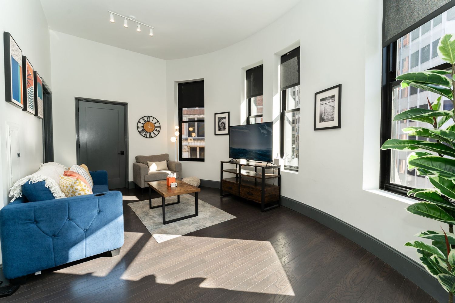Modern living room interior with blue velvet sofa, black framed artwork, and natural light from large windows.