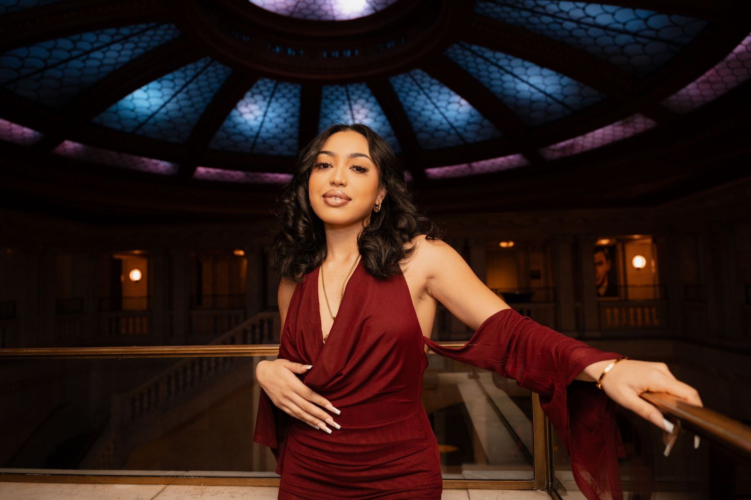 Evening photoshoot in elegant burgundy dress against dramatic indoor lighting.