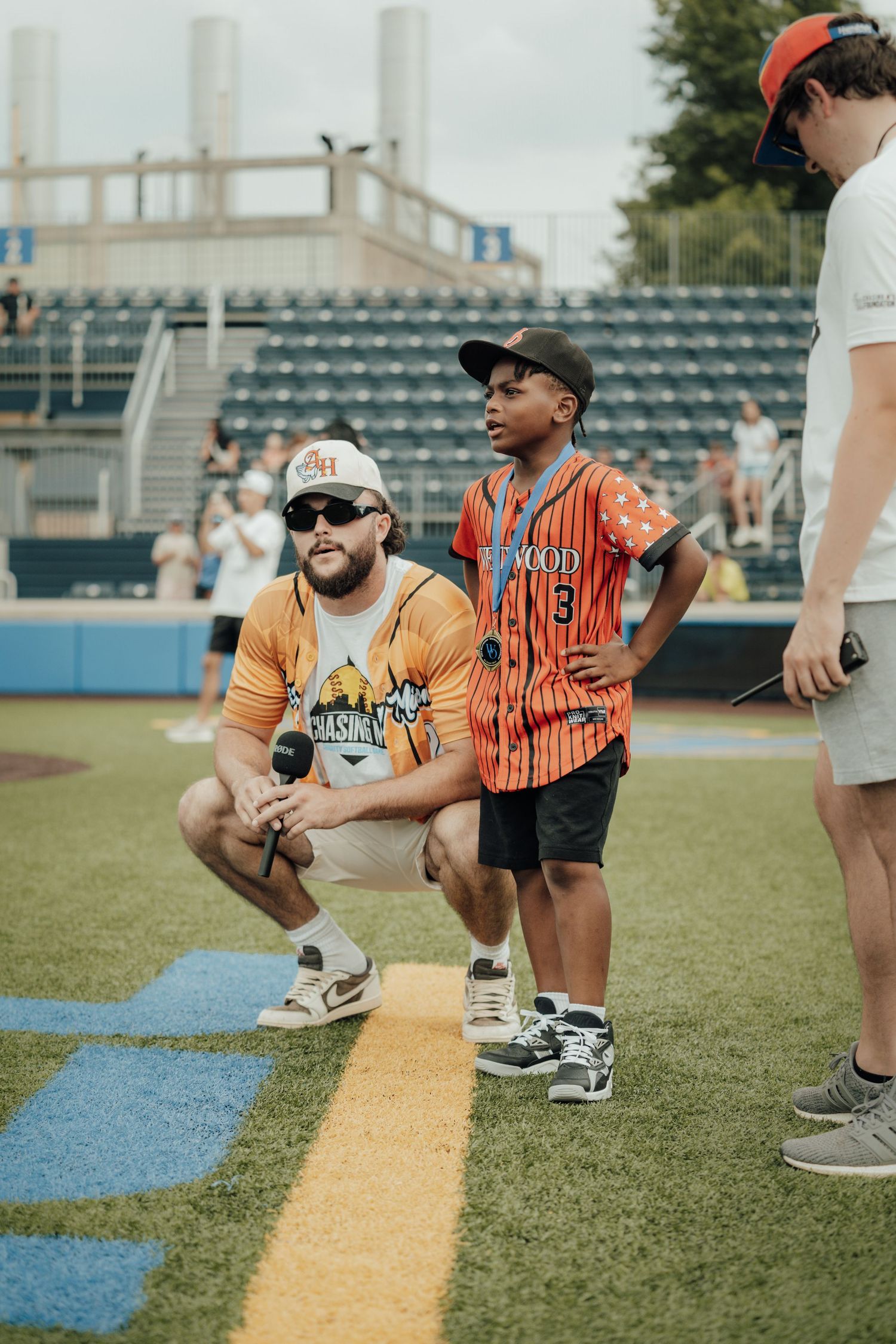 Baseball players gather on a sports field near the foul line at a stadium with empty bleachers in the background.