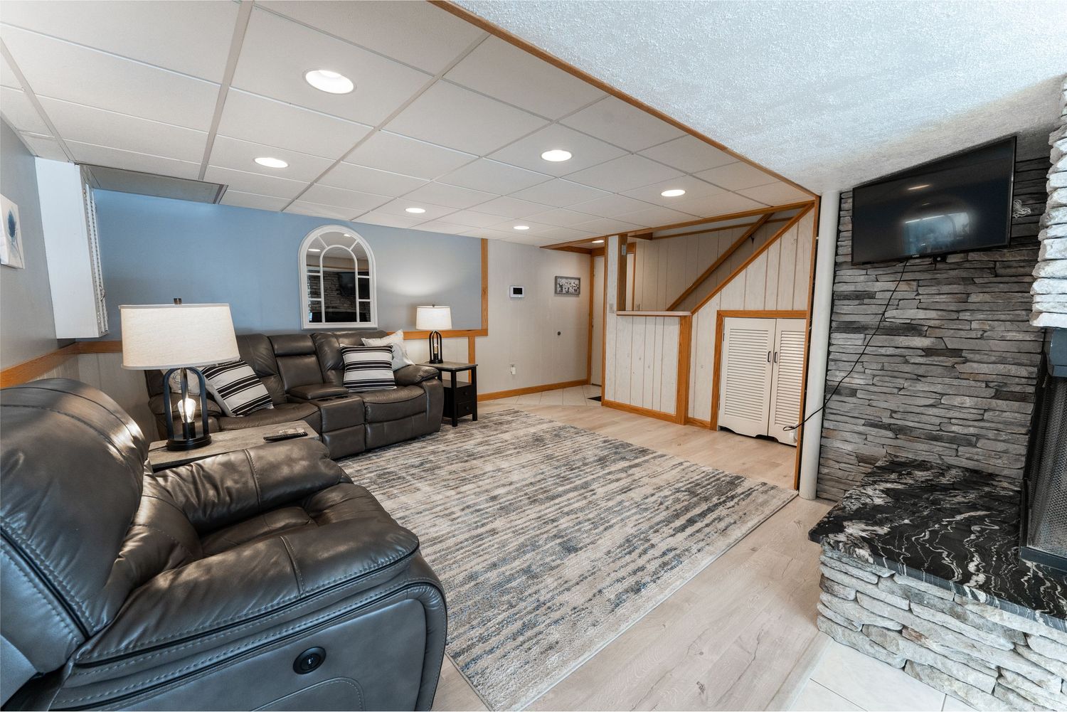 Modern basement remodel features gray wood-look flooring, recessed lighting, and stone accent walls throughout the space.