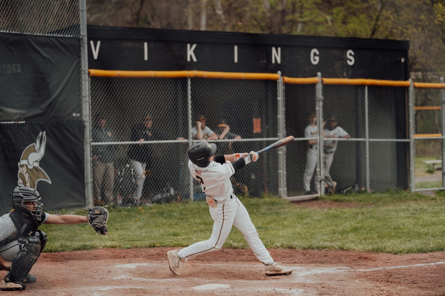 baseball player swings at a pitch during a Vikings home game with fielders visible in background.