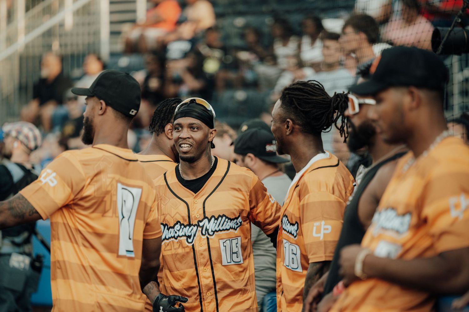 Baseball team members in bright orange jerseys share a lighthearted moment in the dugout during a game.