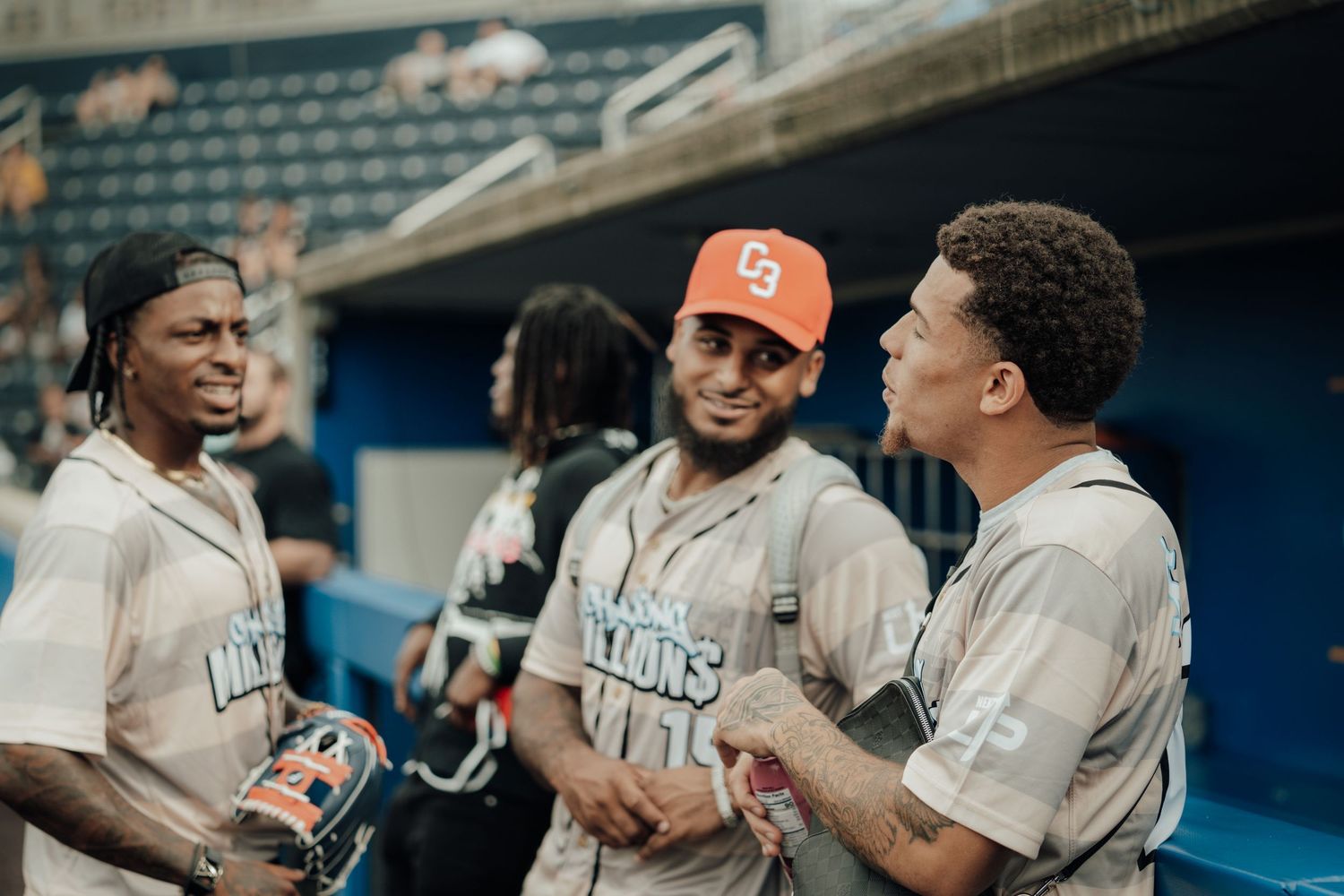 Three Detroit Stars teammates in gray uniforms having a conversation in the dugout during a baseball game.