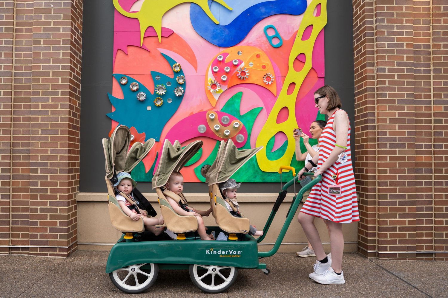 A red wagon sits in front of a colorful abstract mural on a brick wall.