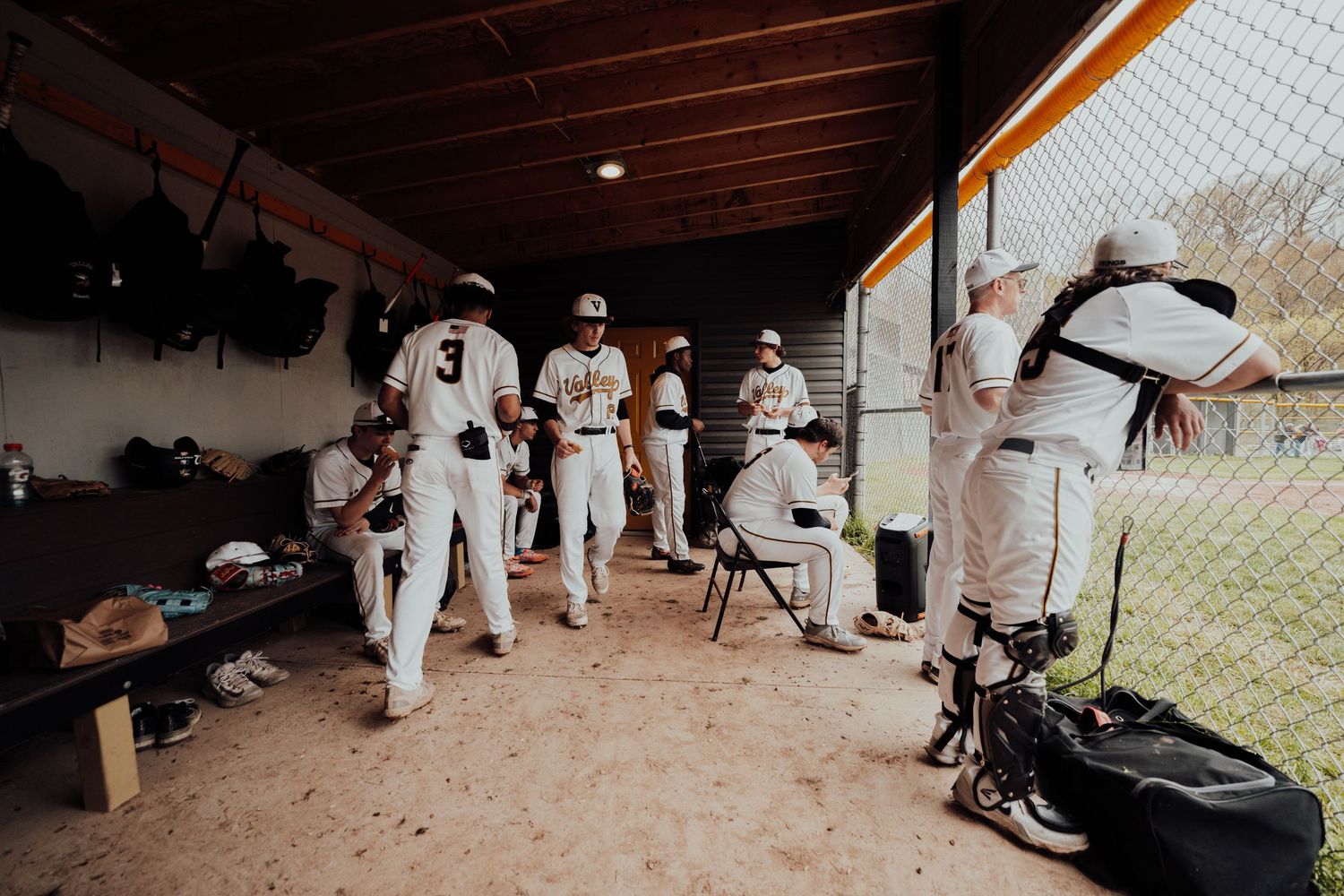 Baseball players in white uniforms wait in dugout during game.