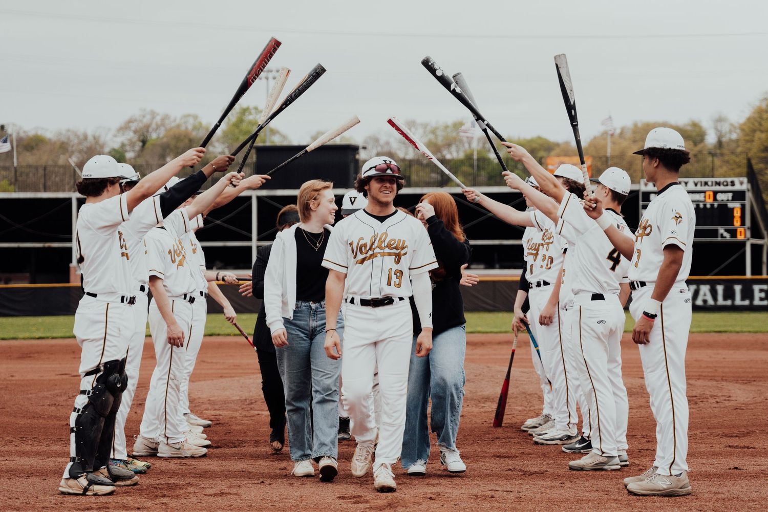 Baseball players line up in white uniforms forming a procession along an outdoor field during a sports ceremony.