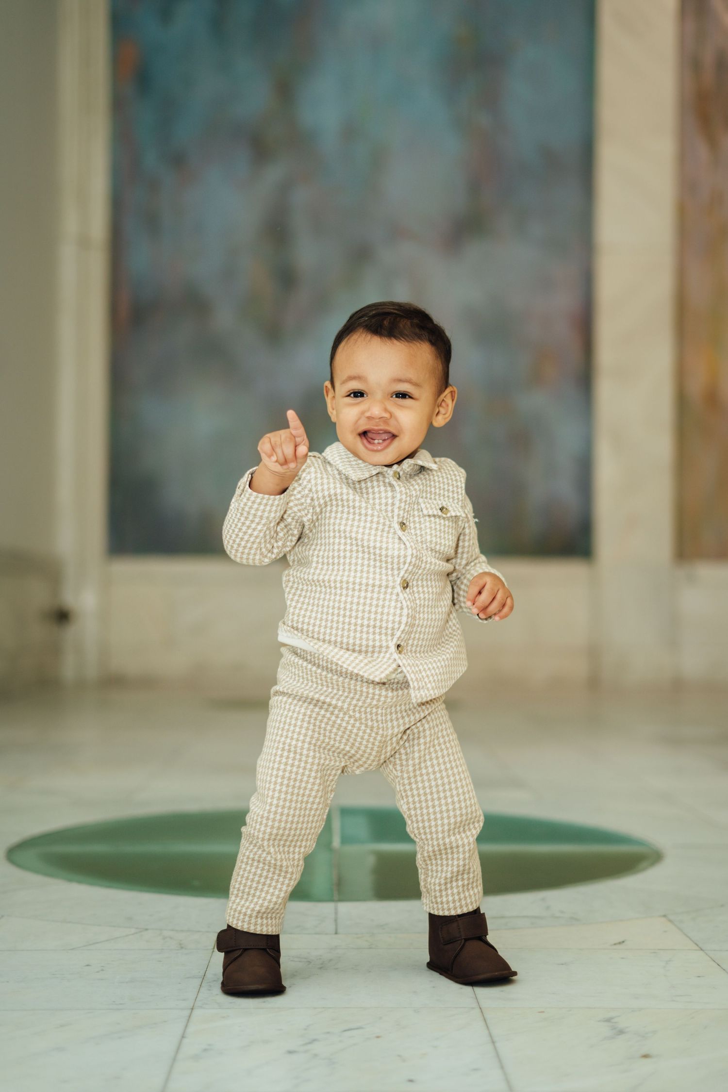 Adorable baby in checkered outfit dances and smiles in series of joyful poses on marble floor.