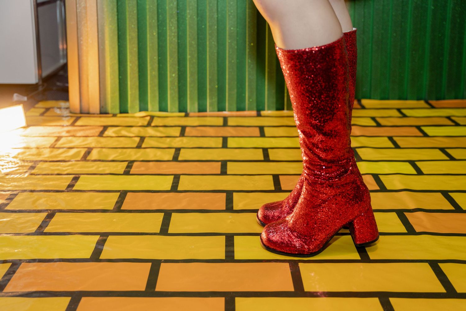 Sparkly red boot stands on yellow brick road floor design.