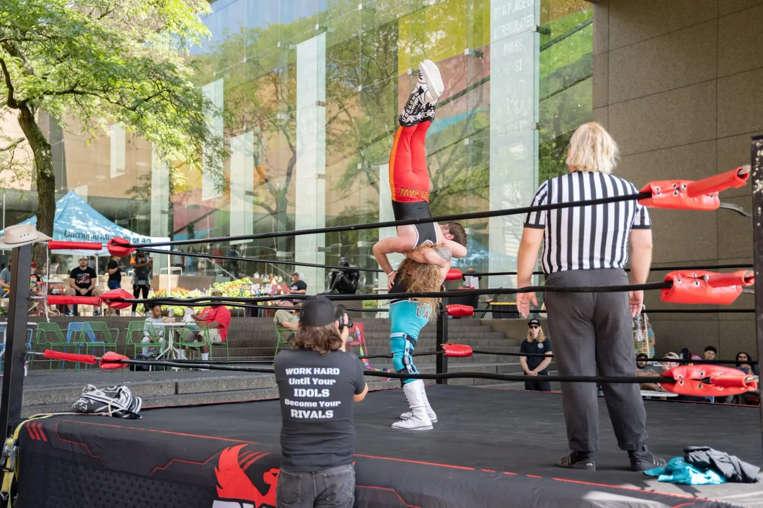 Wrestling ring set up outdoors with referee and performers during a sunny day event.