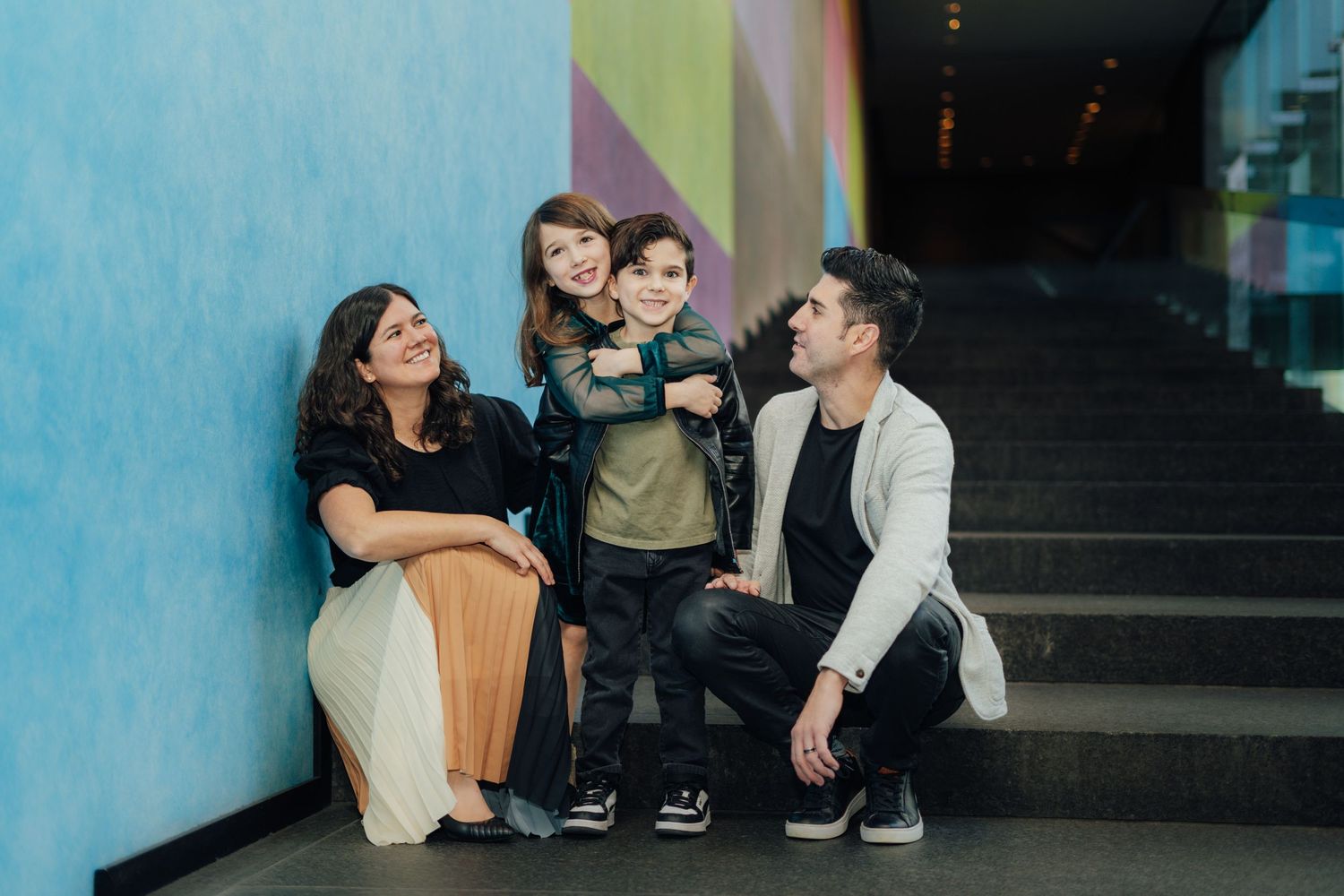 A group sits together on concrete steps against a blue wall in an urban setting.