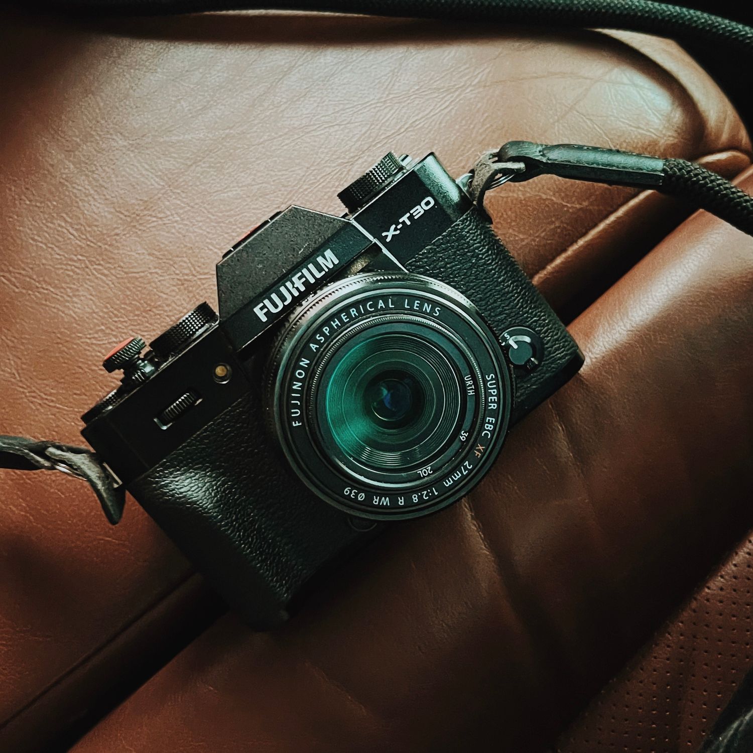 Fujifilm camera with black body and green lens sitting on brown leather surface.