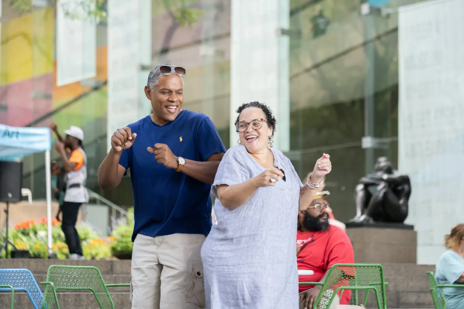 People gathered and conversing near modern green benches outside an urban building.