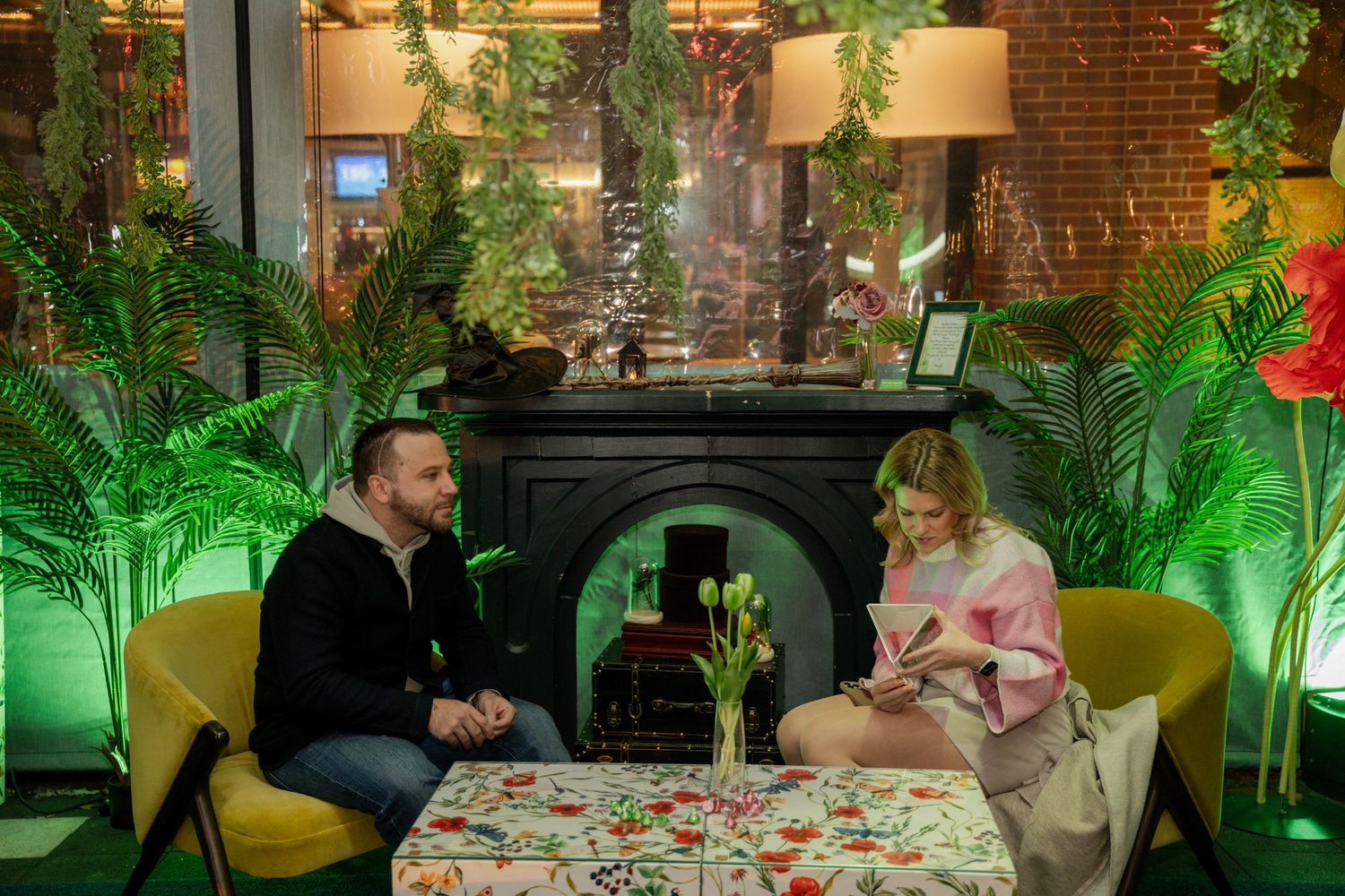 Two people enjoying drinks at a cozy restaurant table surrounded by lush green plants and ambient lighting.