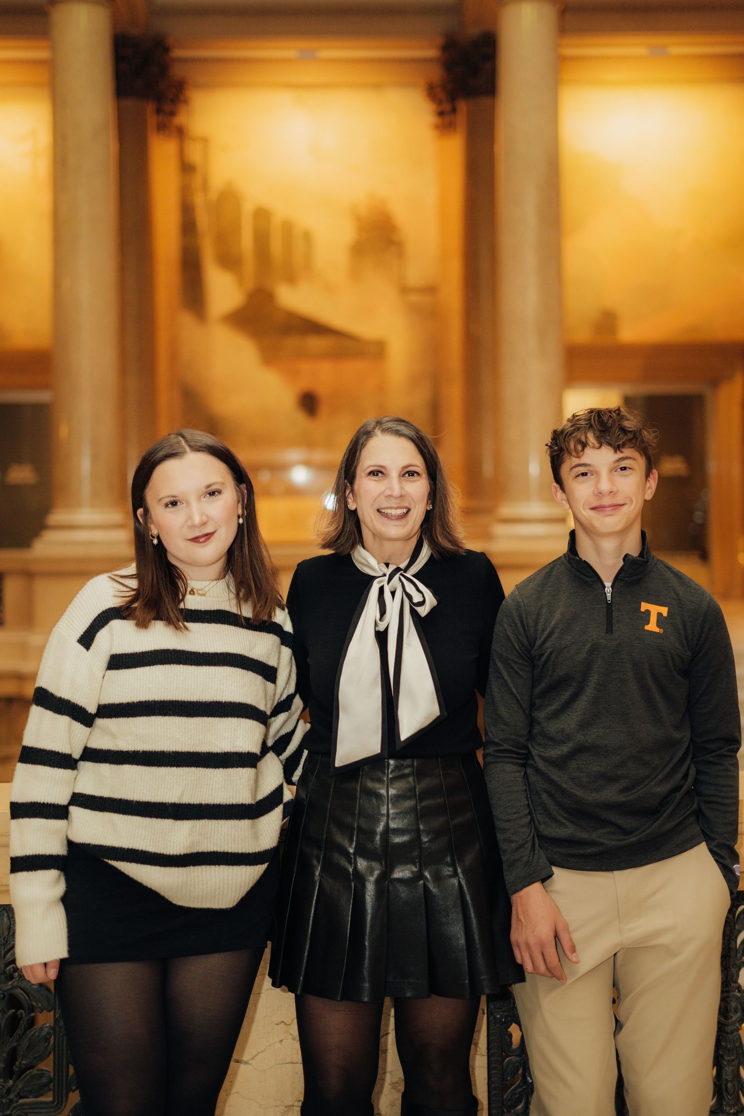 Group photo in formal attire standing in warmly lit classical hallway.