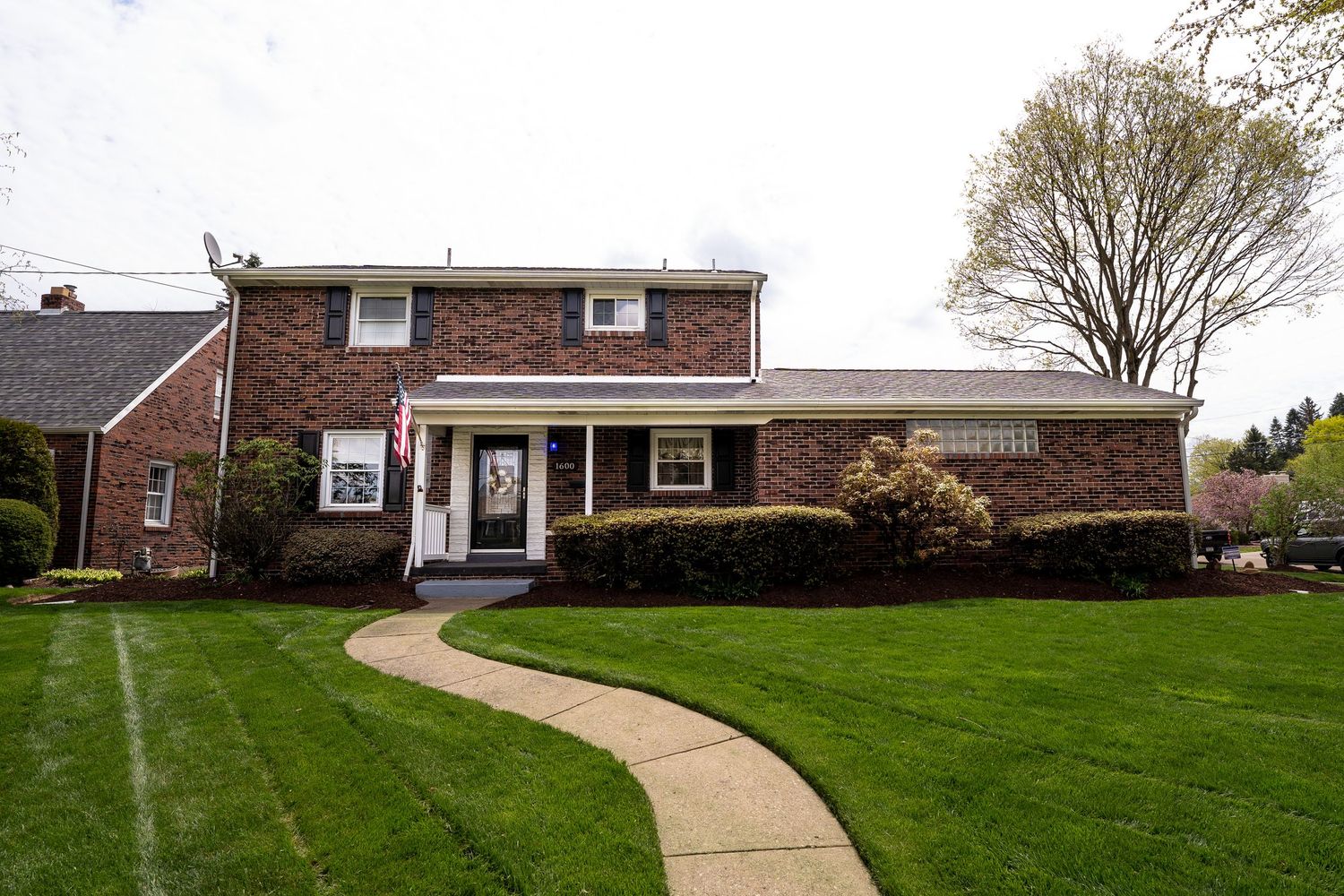 A curved concrete walkway leads to a brick ranch-style house with white trim and a manicured green lawn.