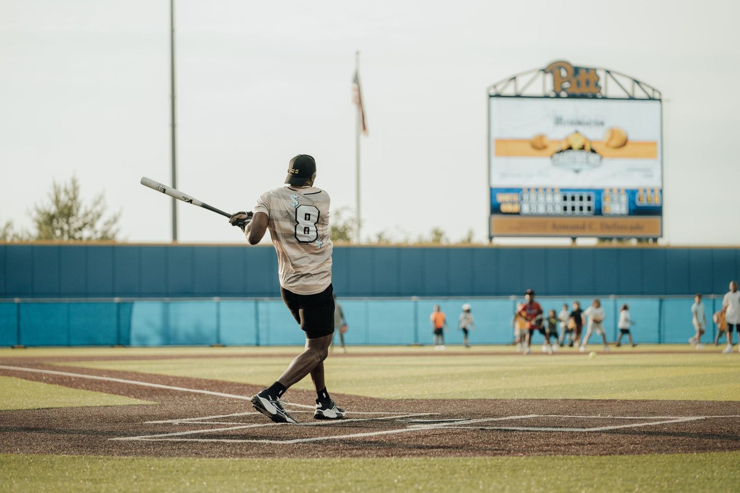 Baseball batter in white jersey with number 38 stands at home plate ready to swing on a sunny day at a baseball field.