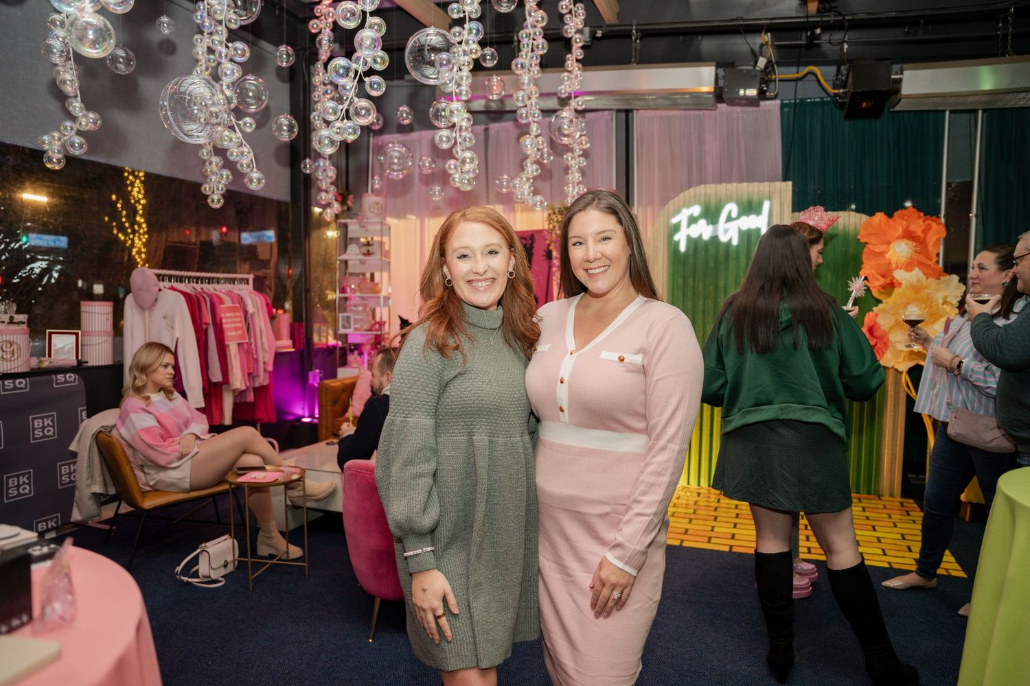 Group of people enjoying a social event at a retail store with green and pink decor elements in background.