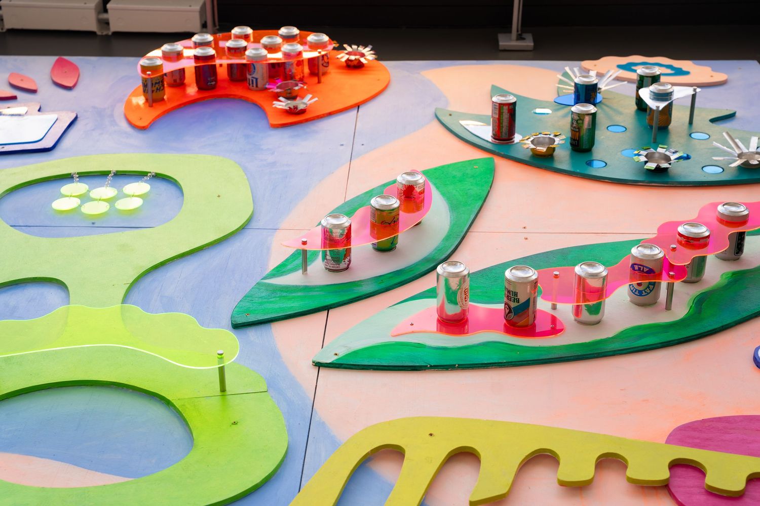 Small shot glasses arranged on colorful leaf-shaped platforms display vibrant drinks at a catering event.
