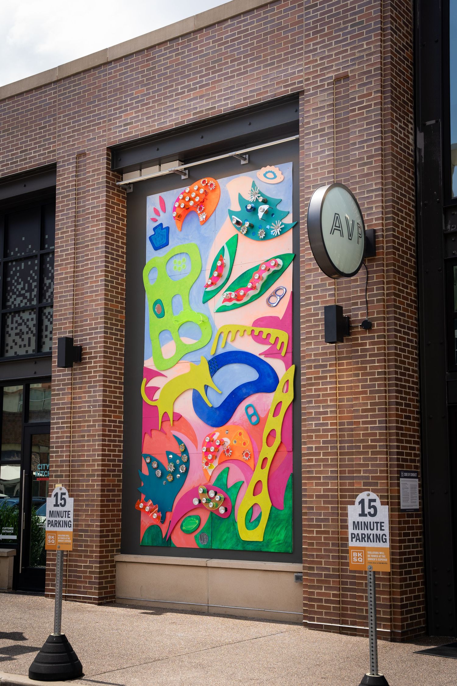 Colorful abstract mural with vibrant swirling patterns displayed on brick building storefront windows.