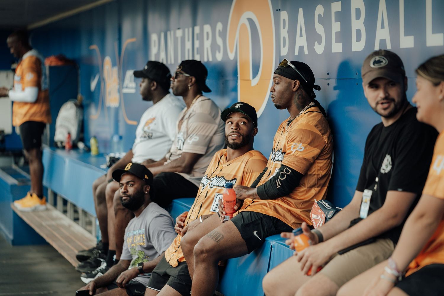 Baseball players sit in the dugout during a game wearing navy blue uniforms with matching caps.