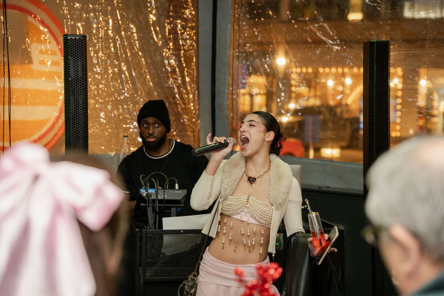 People enjoying a lively karaoke performance at a party with string lights and decorations in the background.