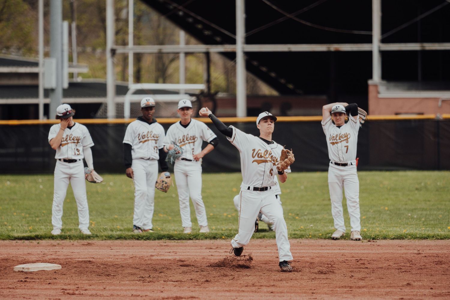 Baseball players in white uniforms line up along the infield dirt during a game.