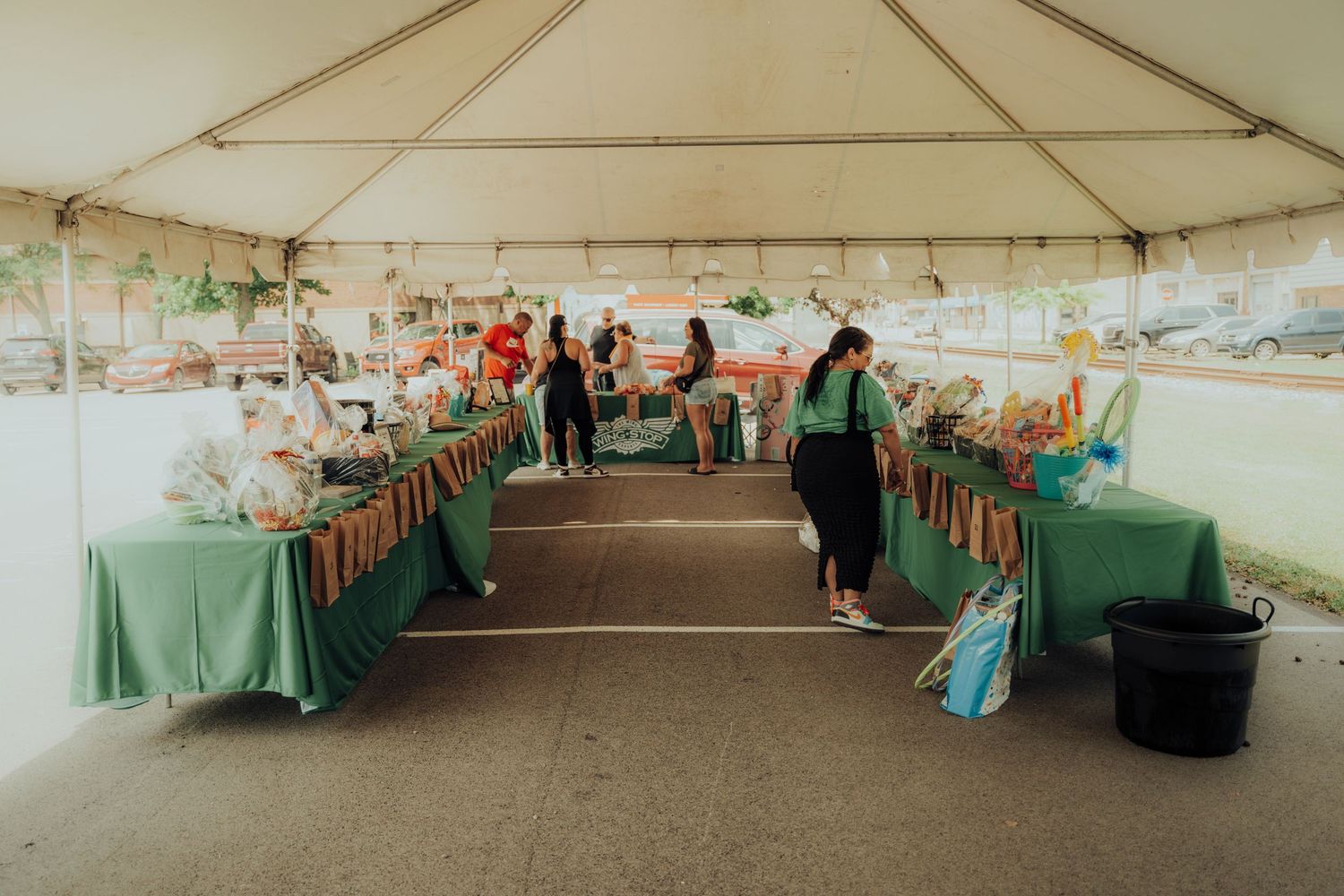 Event vendors display their wares at tables covered in mint green tablecloths under a large white outdoor tent.