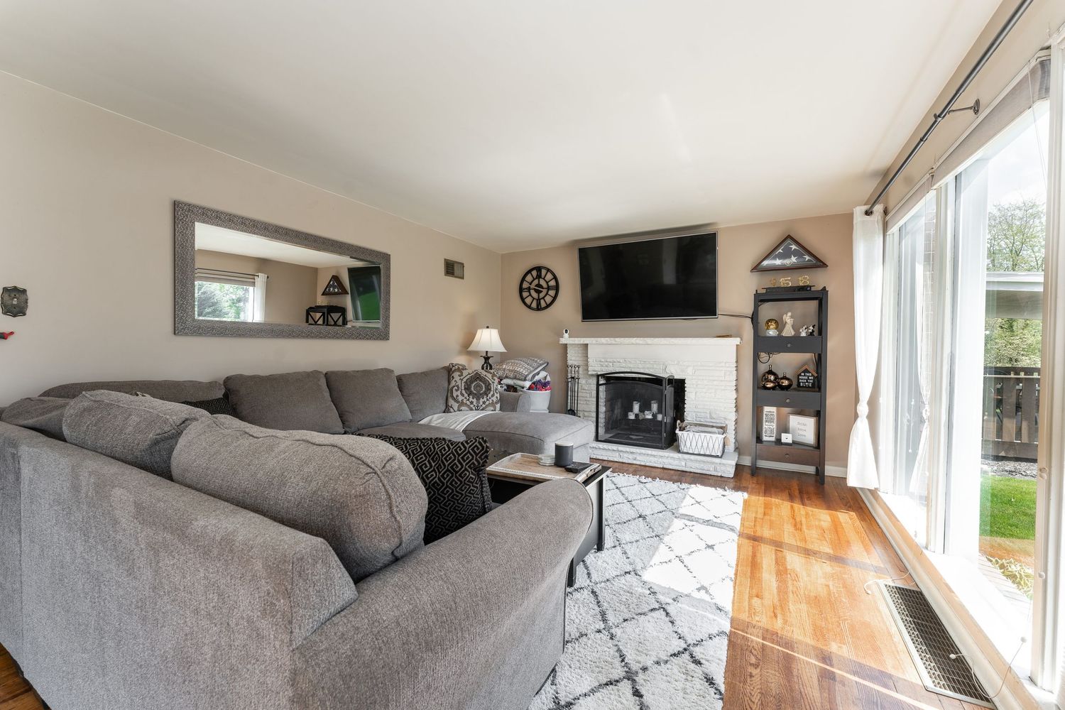 A modern living room features a gray sectional sofa, large windows, and natural light streaming in.