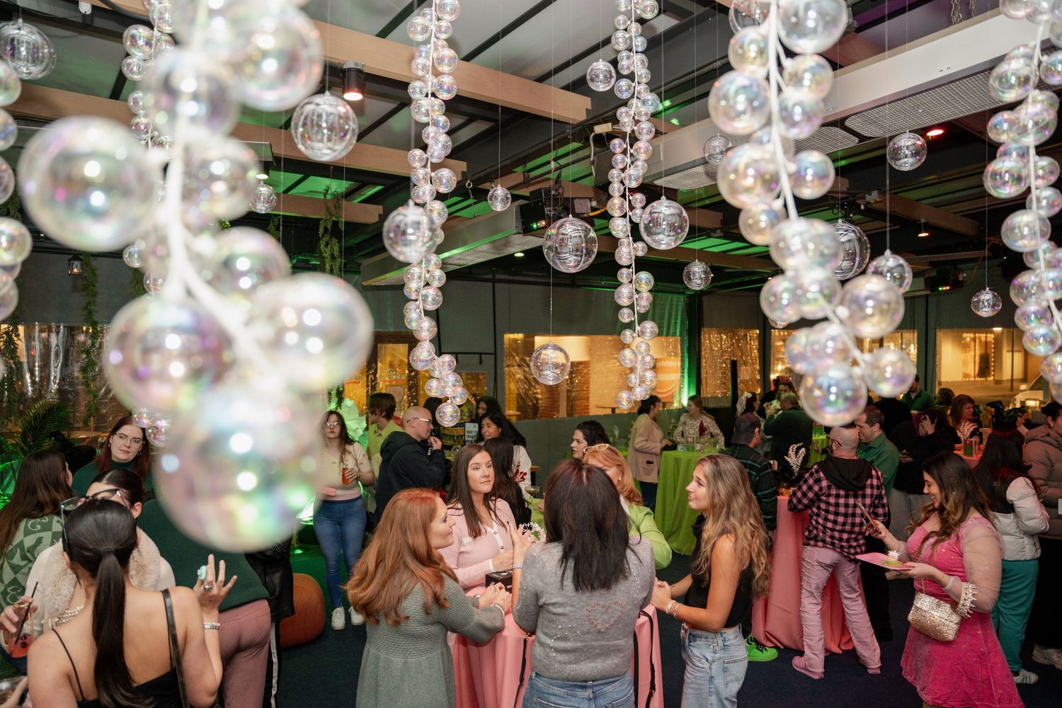 Partygoers celebrate under hanging iridescent bubble decorations and crystal strands in a festively lit venue.