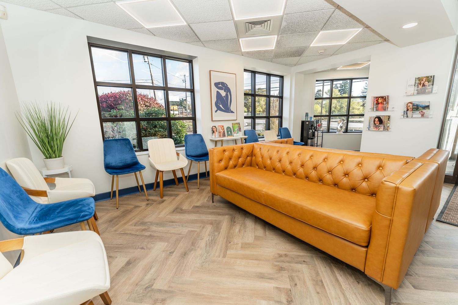 Contemporary office interior with tan leather couch, blue accent chairs and hardwood floors in open concept space.