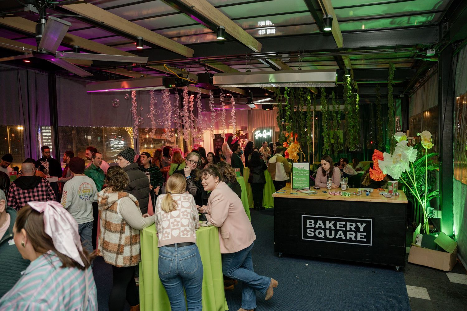 People gathering in a dimly lit indoor space with green accent lighting and retail signage.