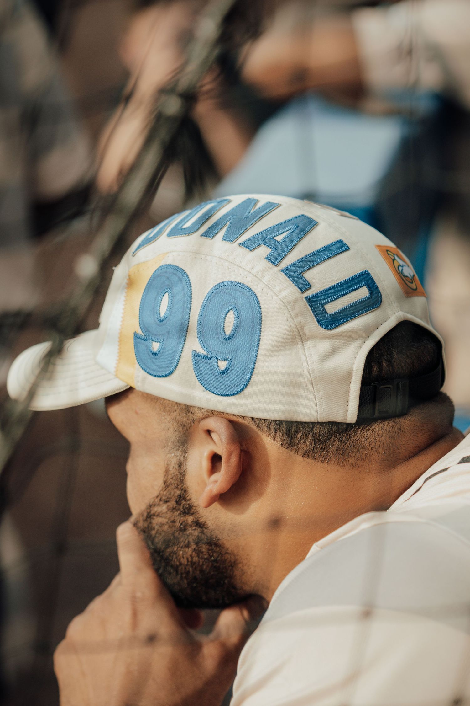 A baseball fan wearing a white cap with the number 99 in light blue lettering during a game.
