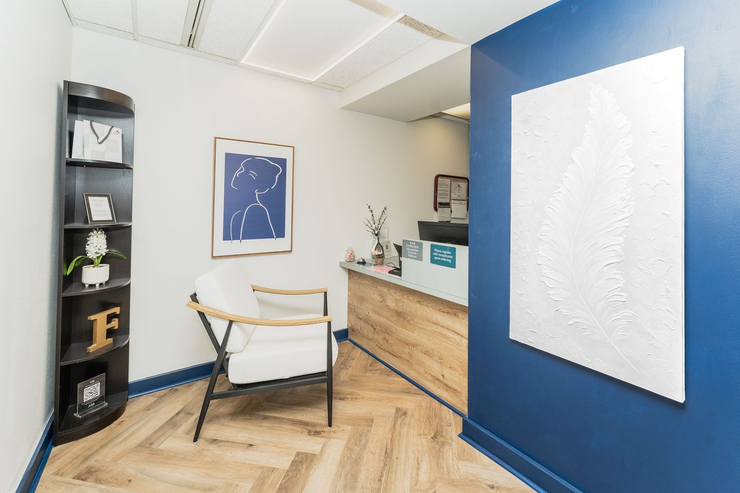 Modern office interior with navy blue accent walls, light wood flooring, and white shelving units displaying decor items.