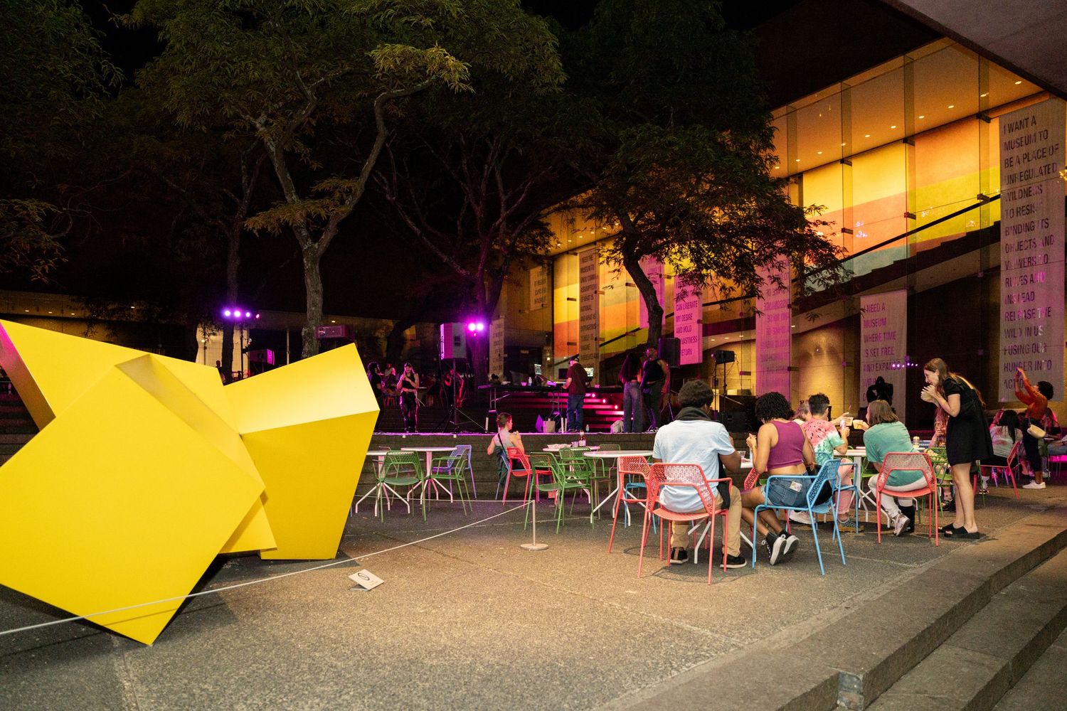 Outdoor evening event space with yellow geometric installations and scattered seating areas.