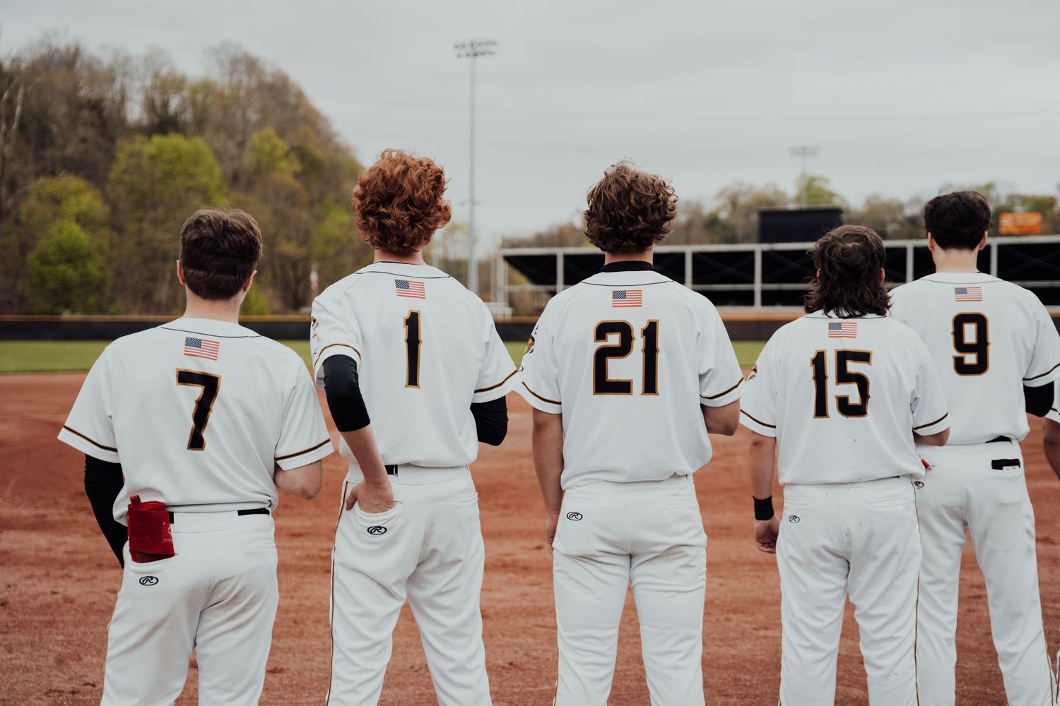 Baseball players stand in line showing their uniform numbers from behind on a baseball field.