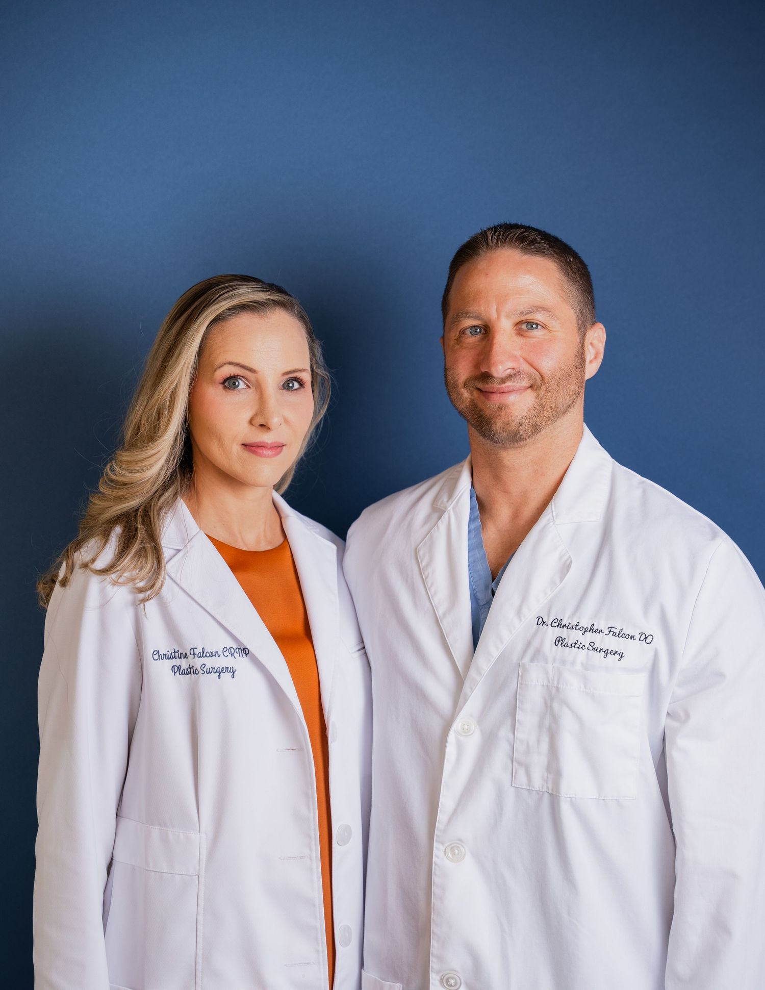 Two medical professionals in white coats stand together against blue background.