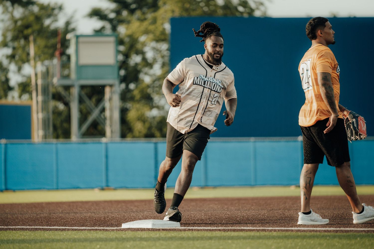 Players practicing on a baseball field during a sunny afternoon with blue walls in the backdrop.