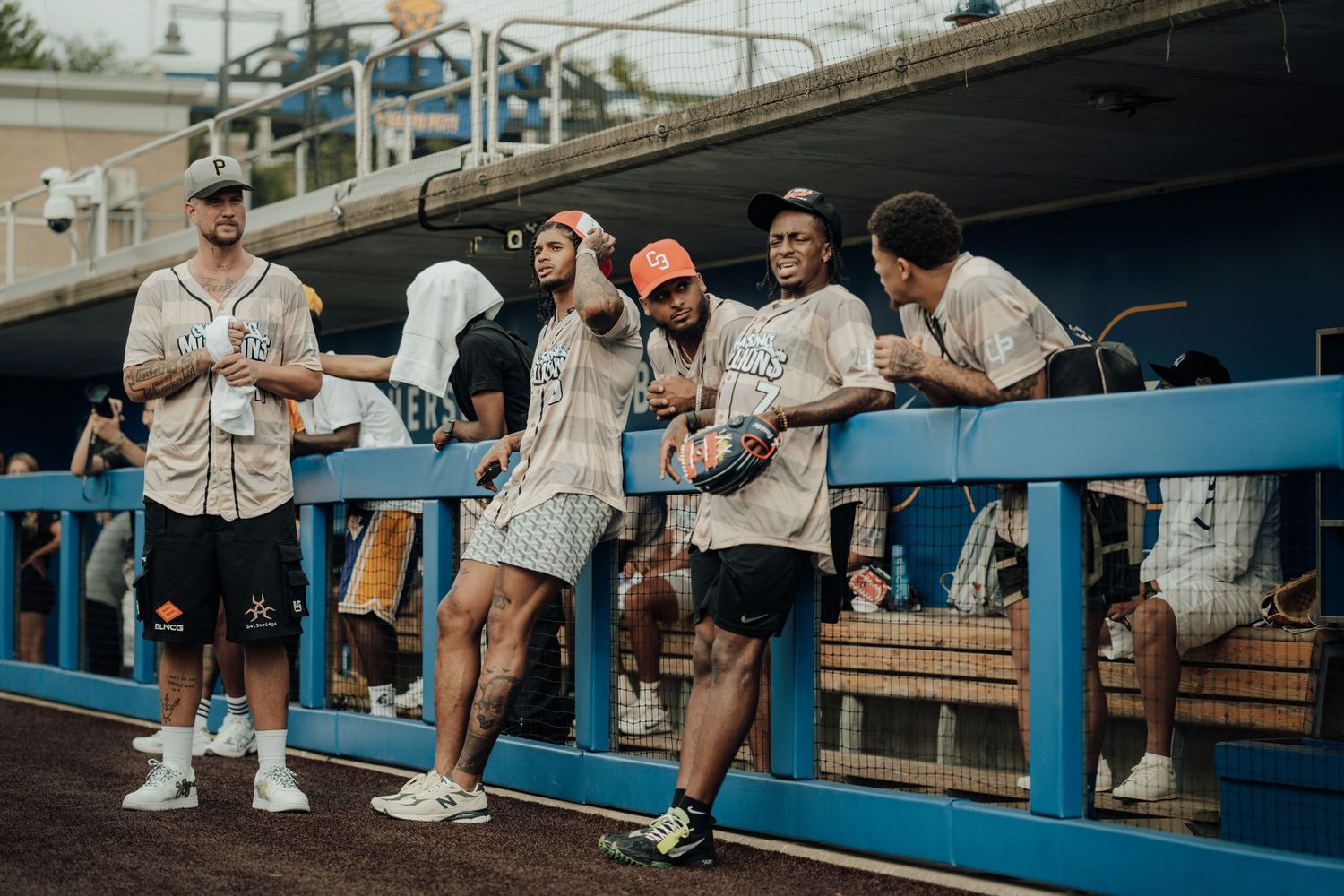 Someone in shorts and sneakers sits on bleachers at a baseball stadium while others watch the game on a sunny day.