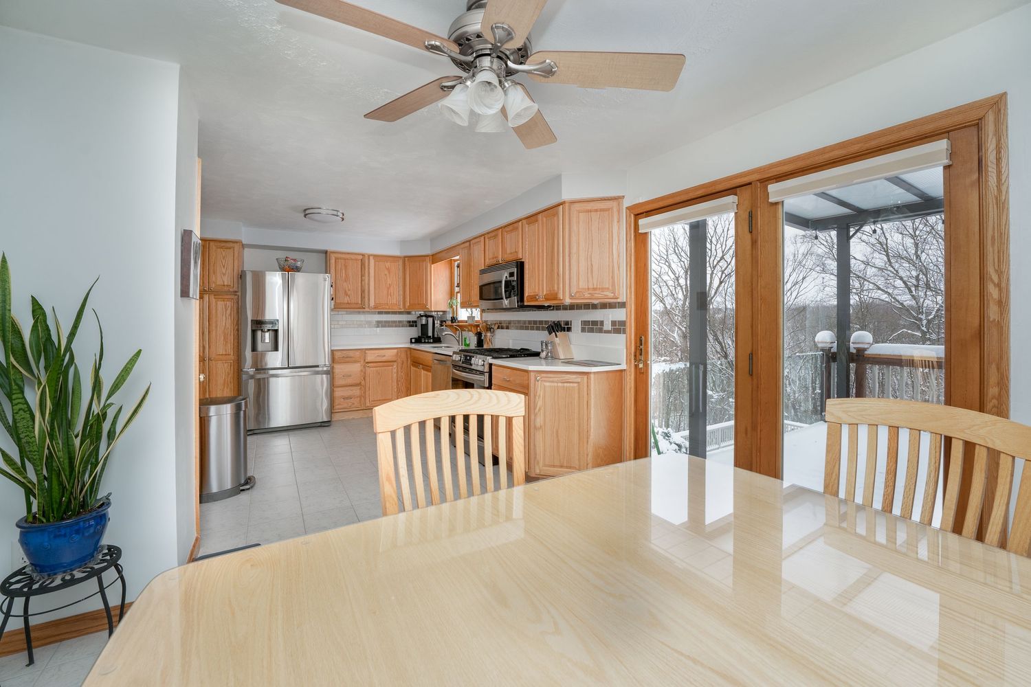 Modern kitchen and dining area with wooden cabinets, stainless appliances and large windows overlooking outdoor deck.