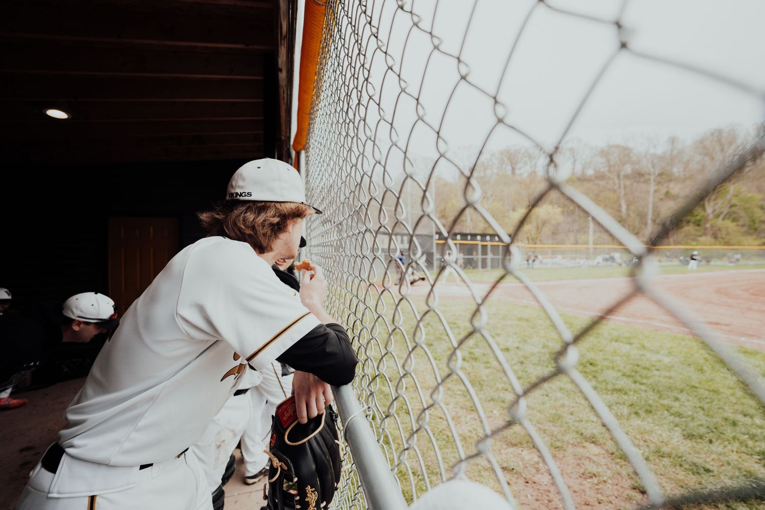 Baseball players observing game through chain link fence at field.