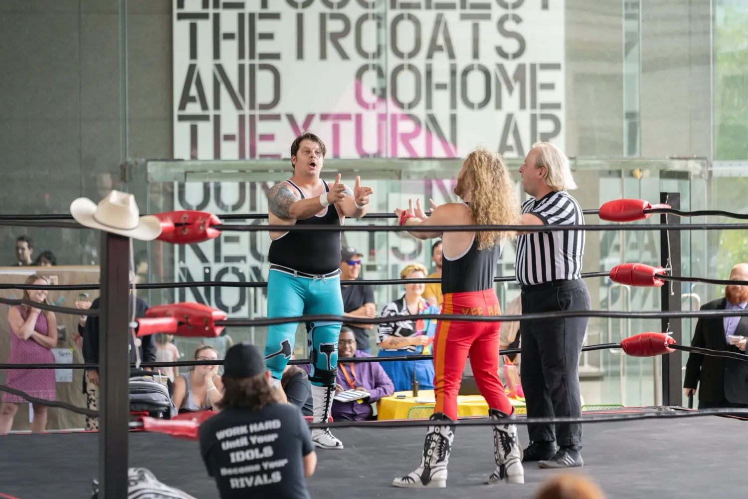 Two wrestlers performing in an outdoor ring while a referee officiates their match.