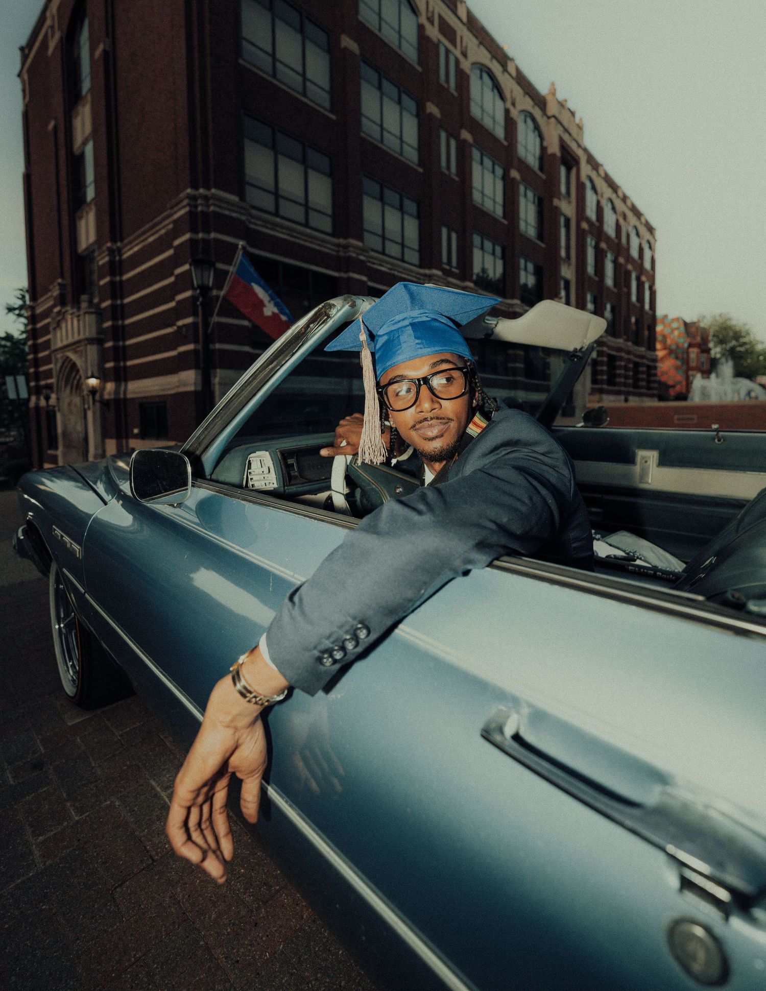 Person in suit and glasses sitting in vintage silver convertible car.