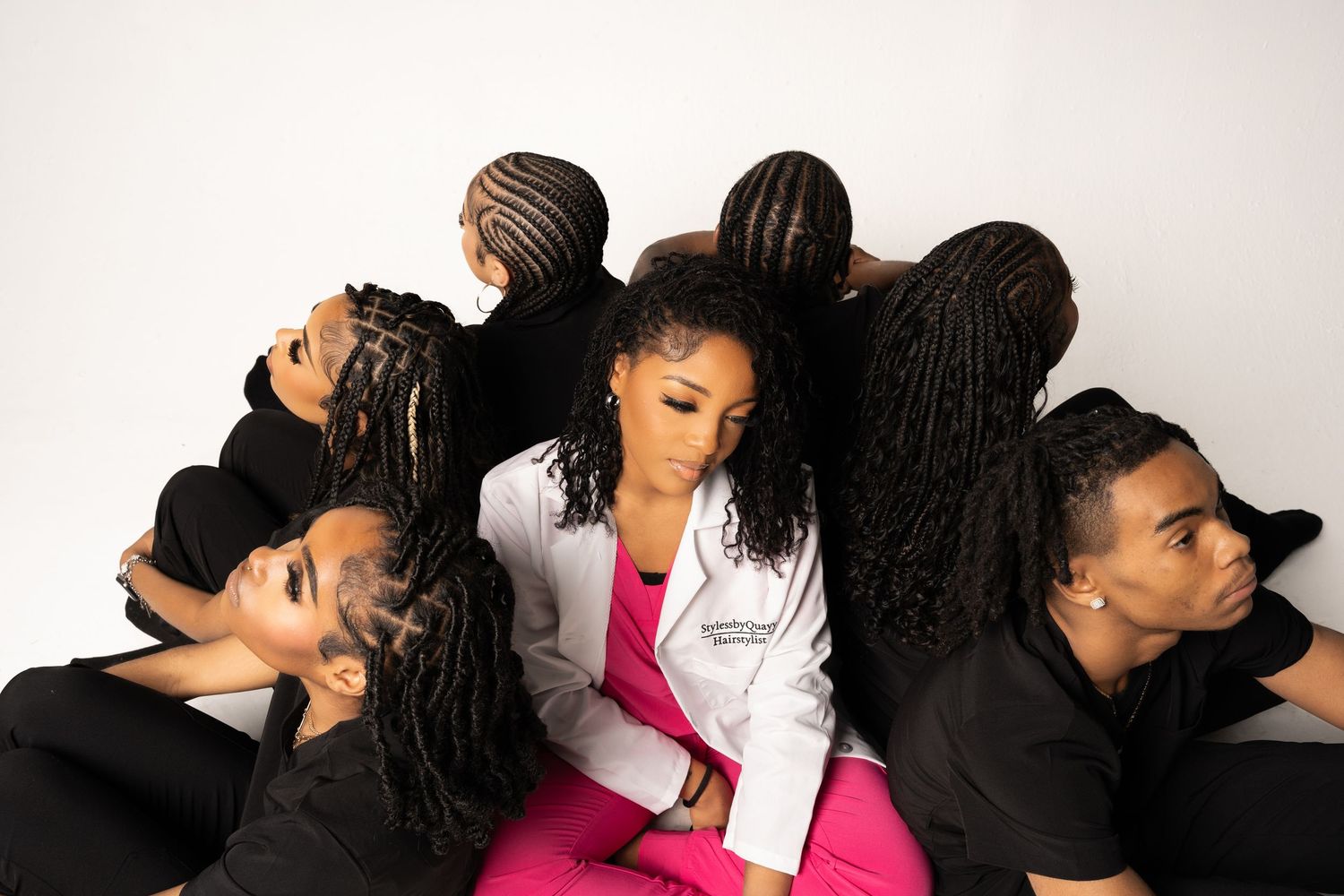 A group photo featuring stylish black outfits contrasting with one person in pink and white medical attire.