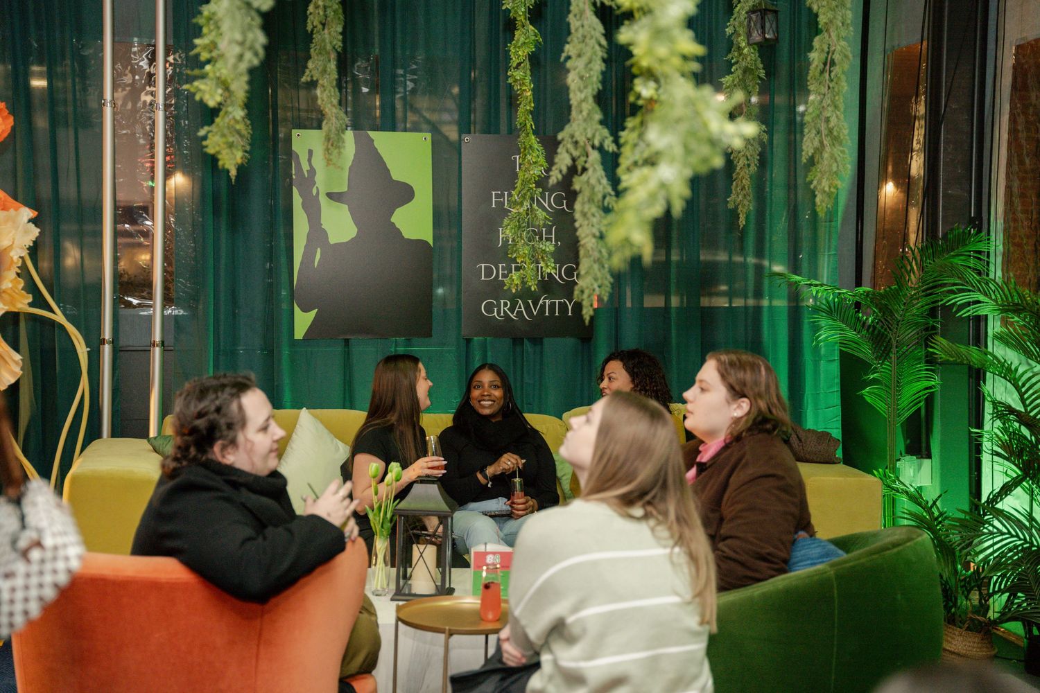 A group chatting and socializing in a cozy lounge space with green decor and ambient lighting.