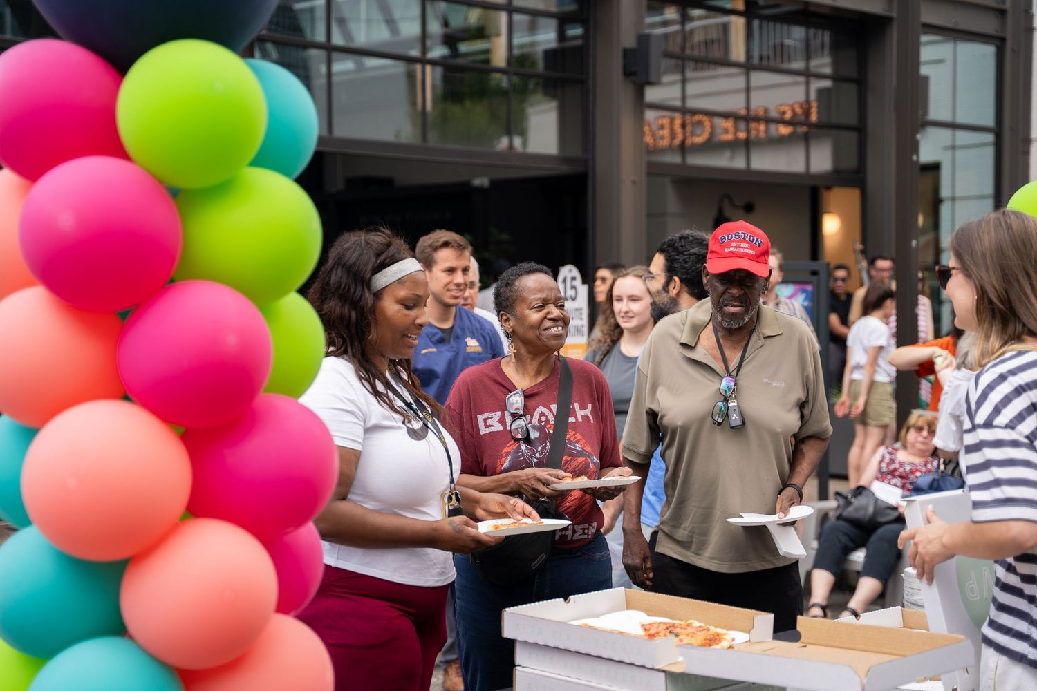 Colorful balloon arch decorates an outdoor gathering with refreshments being served.