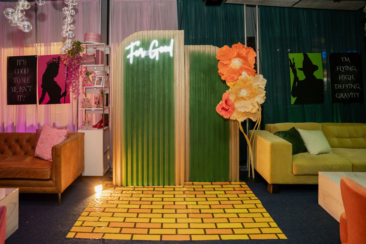 Modern lounge area with neon 'For Real' sign, yellow brick flooring, and orange balloon decorations against green walls.