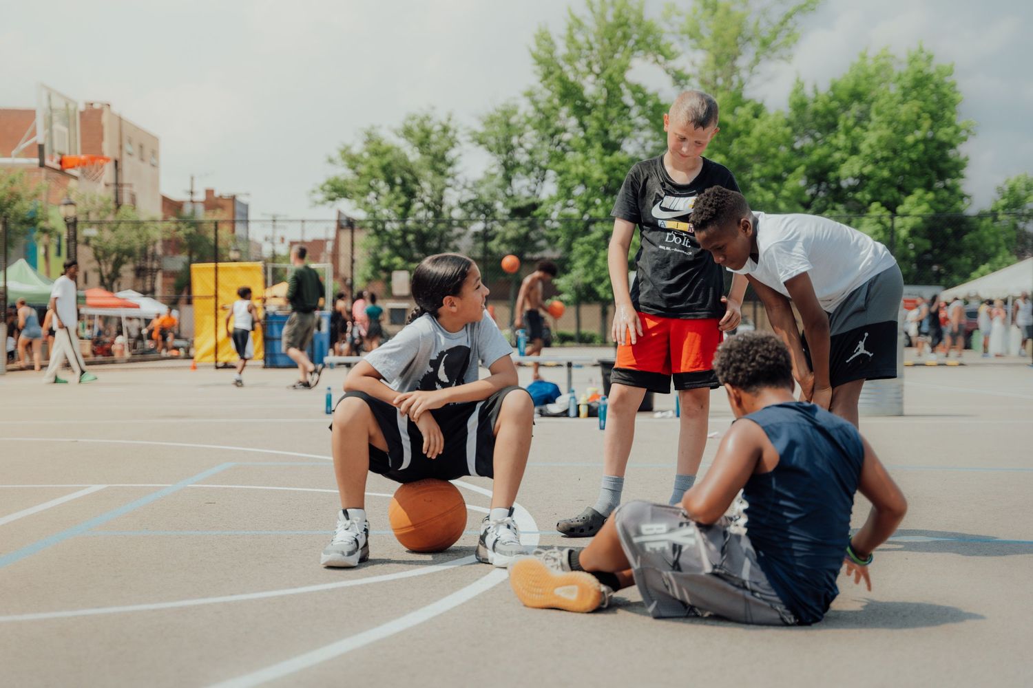 A group of young basketball players taking a break and socializing on an outdoor court during a sunny day.